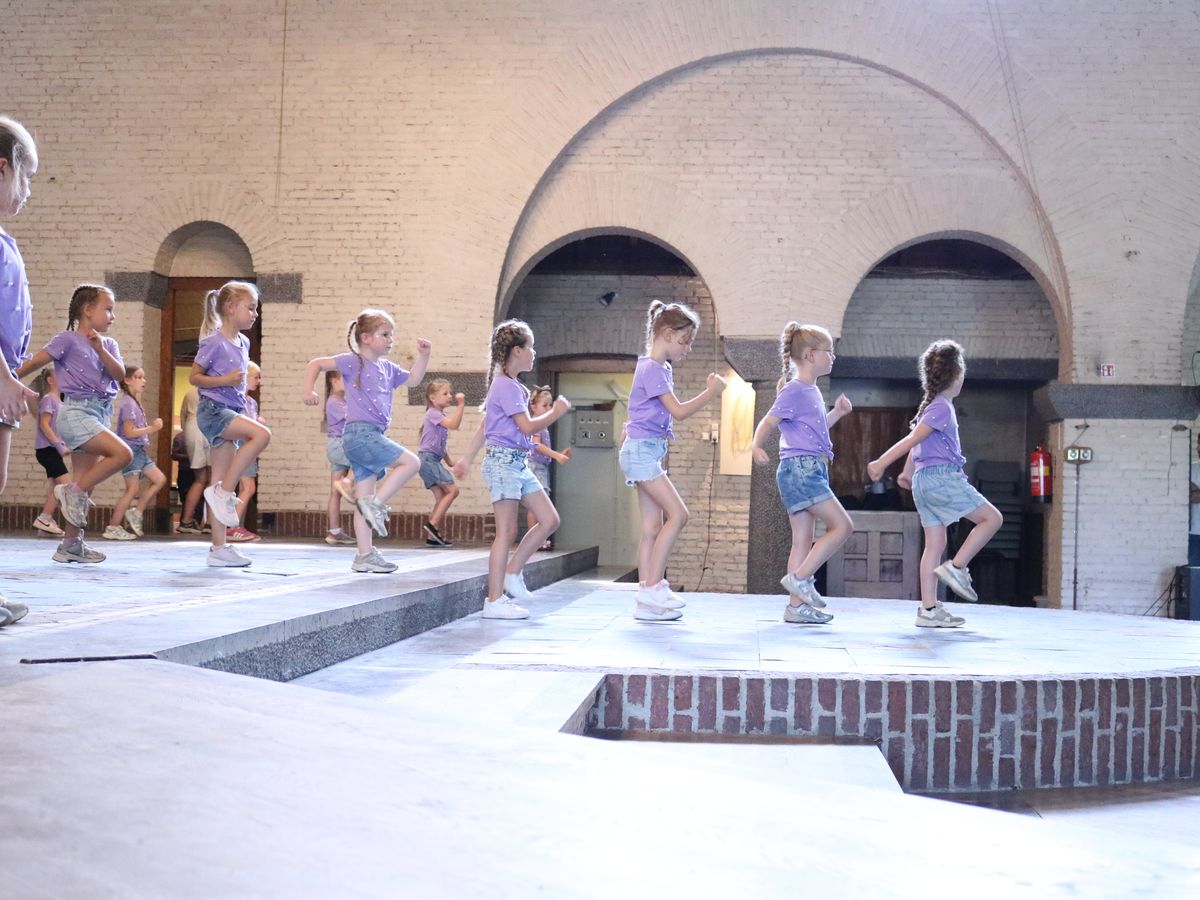Kinderen in paarse shirts dansen achter elkaar over het podium in de kerk.