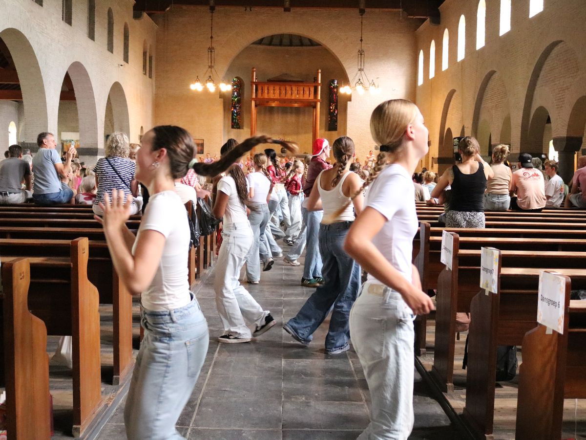 Jonge dansers tussen de kerkbanken tijdens de voorstelling, met publiek erachter.