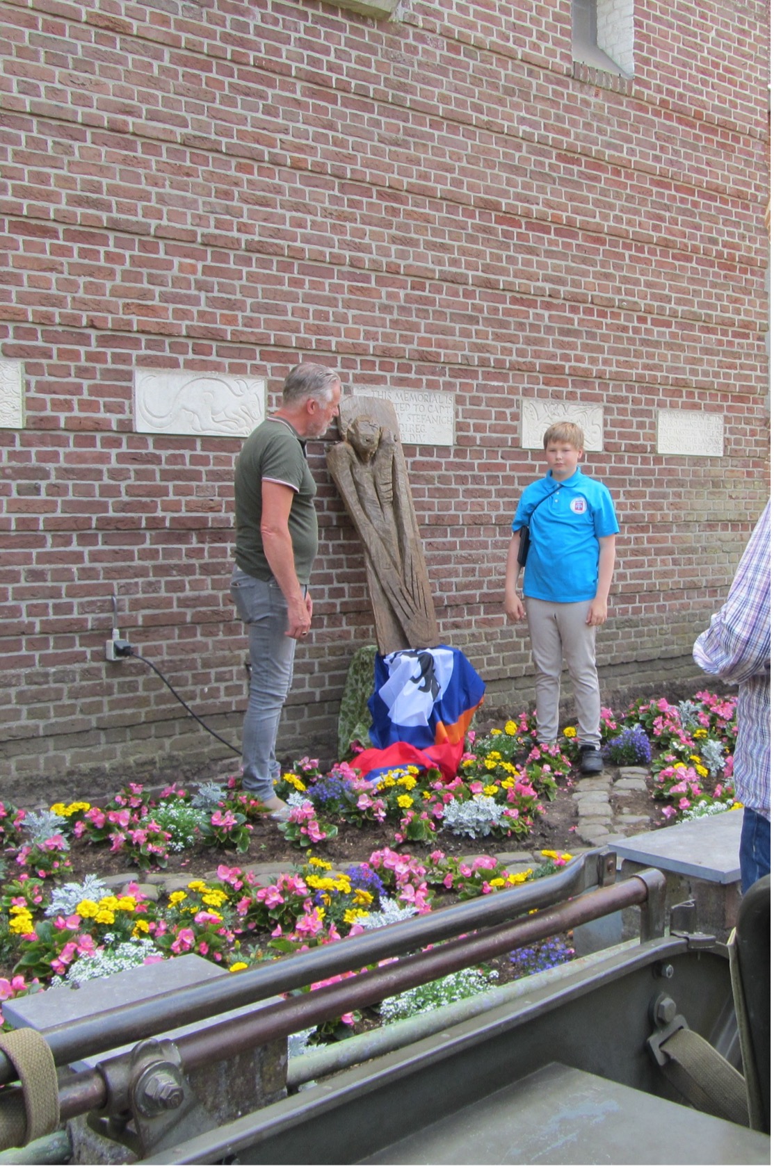 Het houten beeld der tote Soldat tegen de bakstenen kerkmuur.